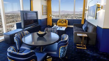 A modern hotel room with a large window, a flat-screen TV, a round dining table, and a sofa.
