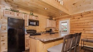 Cocina de cabaña de madera con refrigerador, estufa, microondas y alacenas de madera.
