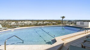 Una piscina con acqua cristallina e blu, circondata da un solarium piastrellato e lettini.