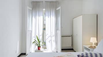 Ein Hotelzimmer mit Bett, Nachttisch, Lampe, Spiegel, Heizkörper und einem Fenster mit Vorhängen.