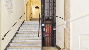 Una scala in marmo conduce a una porta con un cancello in metallo e un segnale di uscita di emergenza rosso.