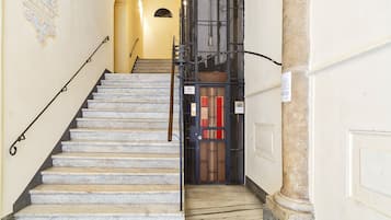 Eine Marmortreppe führt zu einer Tür mit einem Metallgitter und einem roten Feuerschutzausgangsschild.