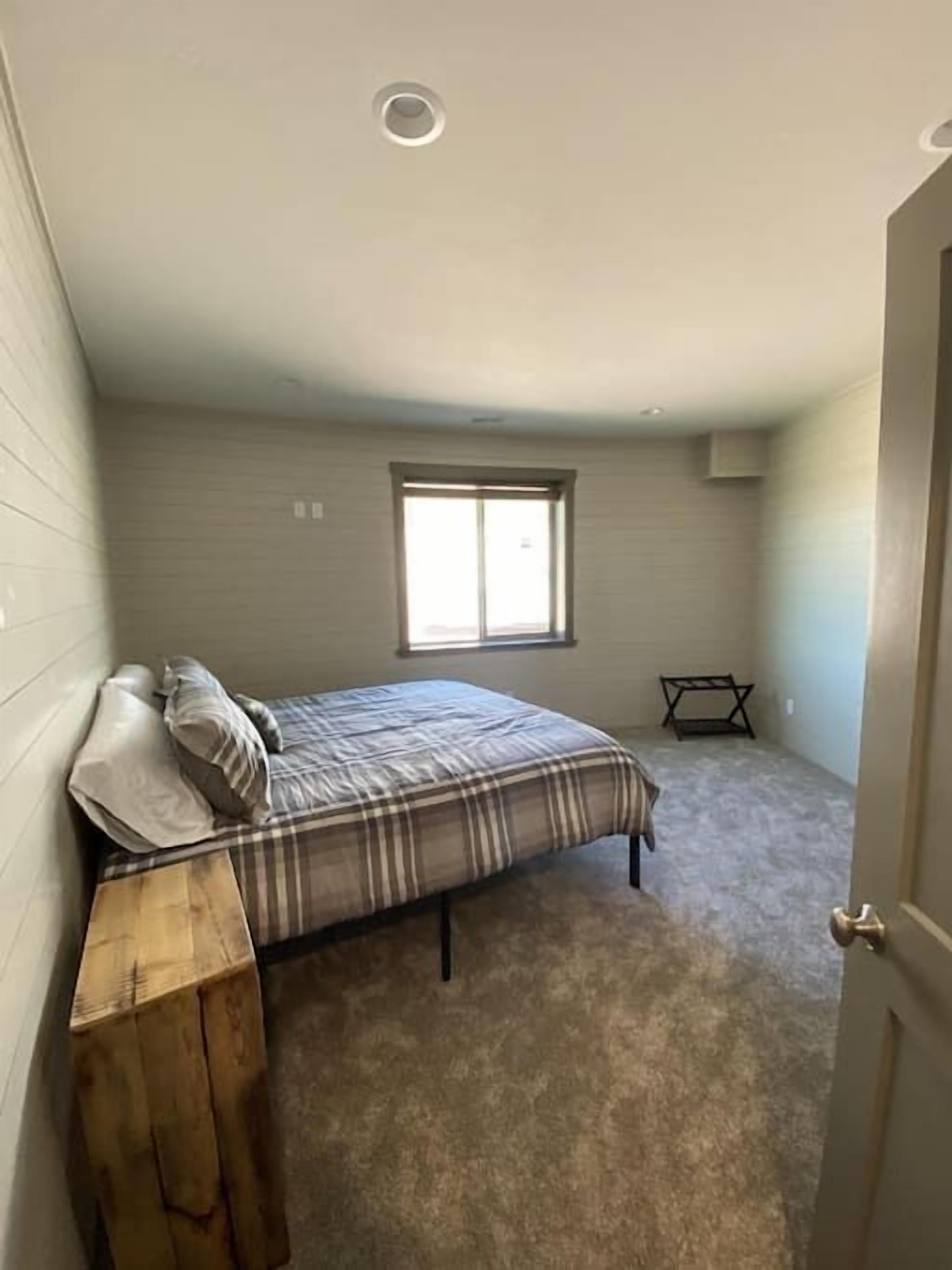 A bedroom with a bed, a window, a small table, and a door.