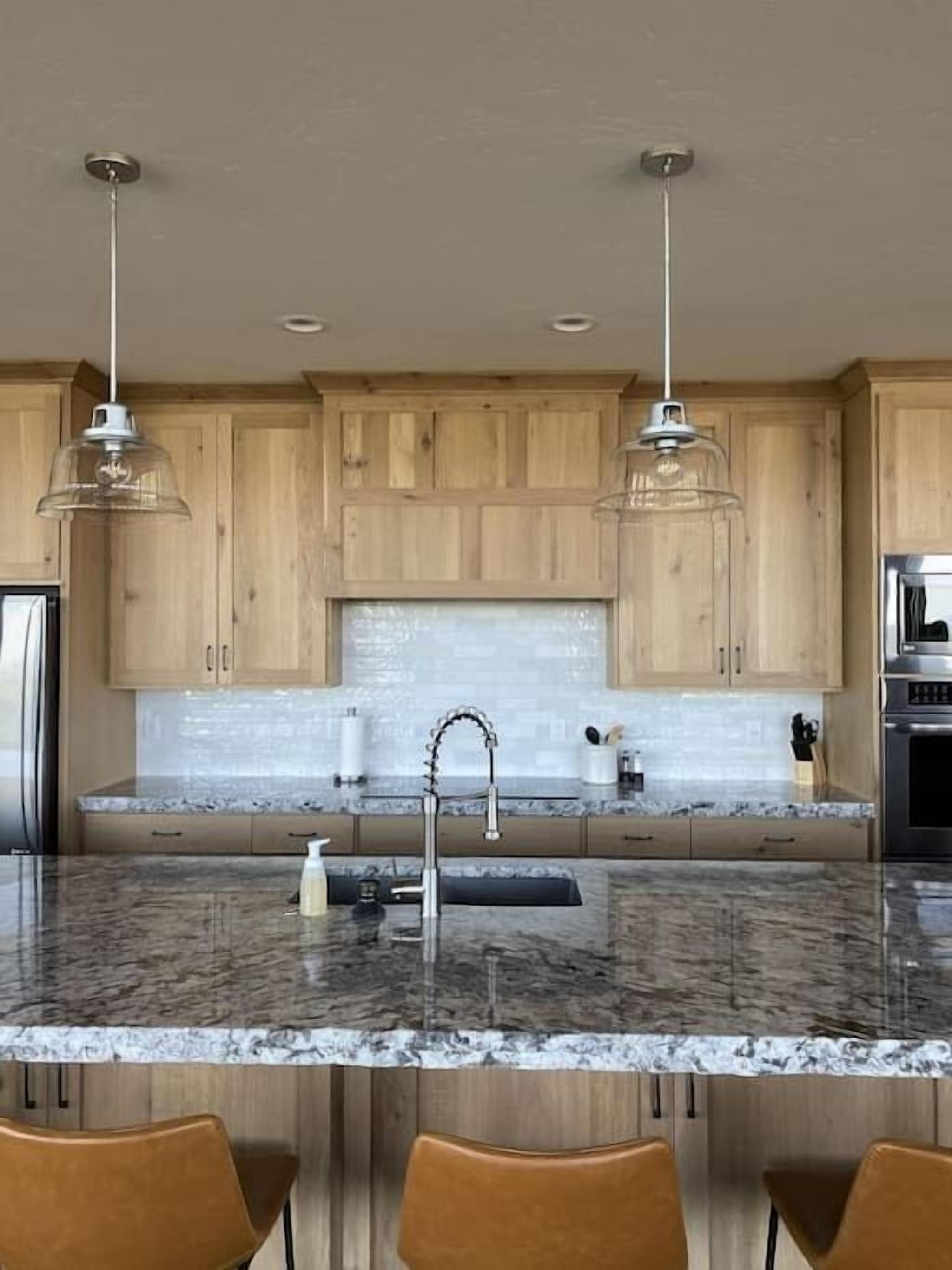 A modern kitchen with wooden cabinets, a granite countertop, a stainless steel sink, and pendant lighting.