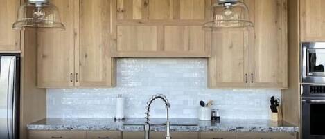 A modern kitchen with wooden cabinets, a granite countertop, a stainless steel sink, and pendant lighting.