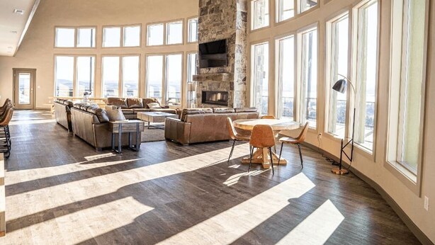 A spacious living room with a stone fireplace, large windows, and a modern sofa set. - 2 Dome Cabins-1 hr to Yellowstone-Hot tub+Theater+Gaming Room+Pool Table+Air Hockey+Shuffle Board+Secret Kids Playroom (Ashton)