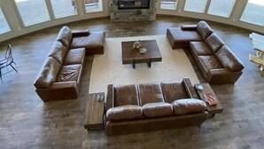 A spacious living room with a stone fireplace, leather sofas, and large windows offering a view of the outdoors. - 2 Dome Cabins-1 hr to Yellowstone-Hot tub+Theater+Gaming Room+Pool Table+Air Hockey+Shuffle Board+Secret Kids Playroom (Ashton)