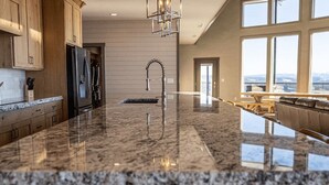 A modern kitchen with granite countertops, stainless steel appliances, and a large window overlooking a scenic view. - 2 Dome Cabins-1 hr to Yellowstone-Hot tub+Theater+Gaming Room+Pool Table+Air Hockey+Shuffle Board+Secret Kids Playroom (Ashton)