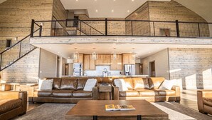 A spacious living area with leather sofas, a wooden coffee table, and a kitchen in the background. - 2 Dome Cabins-1 hr to Yellowstone-Hot tub+Theater+Gaming Room+Pool Table+Air Hockey+Shuffle Board+Secret Kids Playroom (Ashton)