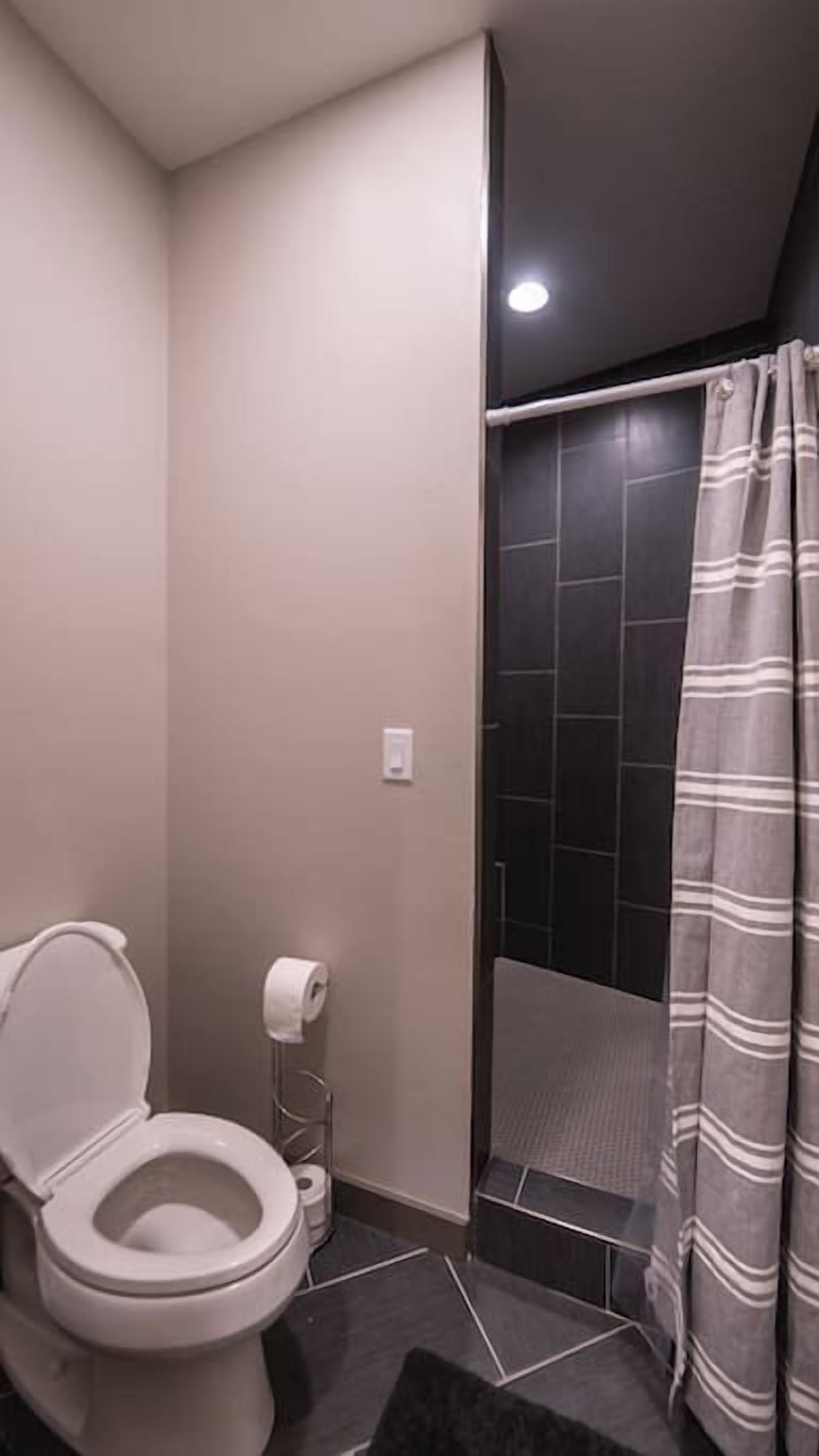 Et badeværelse med toilet, bruser med stribet gardin og fliserede vægge.