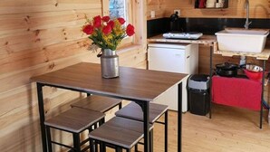 Une cuisine compacte aux murs en bois, avec un petit réfrigérateur, un évier et un coin repas comprenant une table et des bancs.