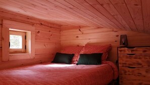 Une chambre dans une cabane en bois, avec un lit, deux oreillers, une commode et une fenêtre.