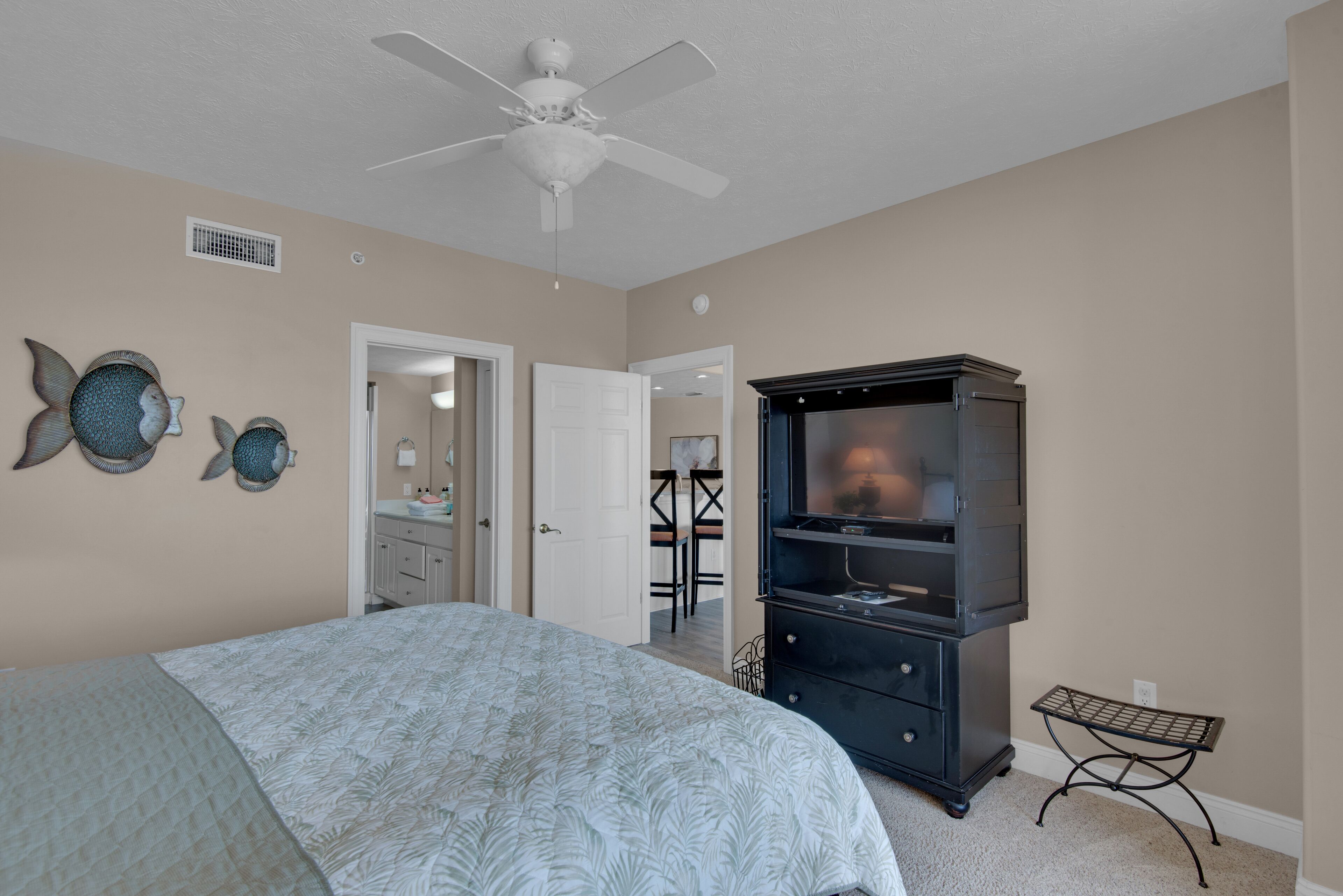 A bedroom with a bed, a ceiling fan, a black entertainment center, and decorative fish wall art.