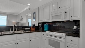 A modern kitchen with white cabinetry, a black countertop, and stainless steel appliances including a stove and microwave.