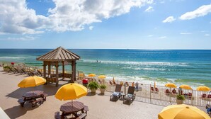A beachside patio with wooden tables and yellow umbrellas, overlooking the ocean.