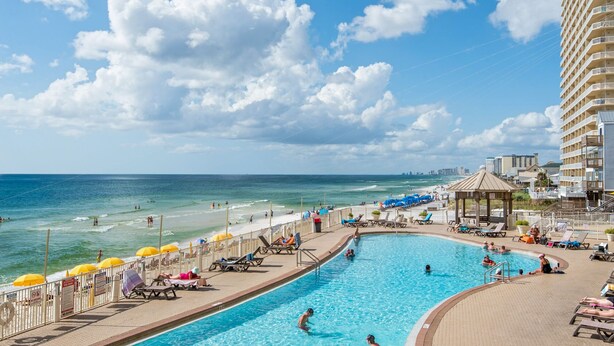 A swimming pool with a view of the ocean and a beach area with umbrellas and lounge chairs.