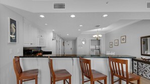 A modern kitchen with white cabinetry, a central island with bar stools, recessed lighting, and a decorative seahorse painting.