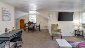 A cozy loft apartment with a dining area, a TV mounted on the wall, and a small side table.