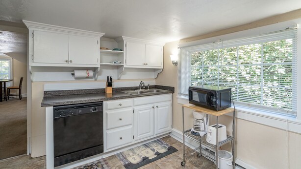 A kitchen with white cabinets, a granite countertop, a dishwasher, a sink, a microwave, and a window with blinds.