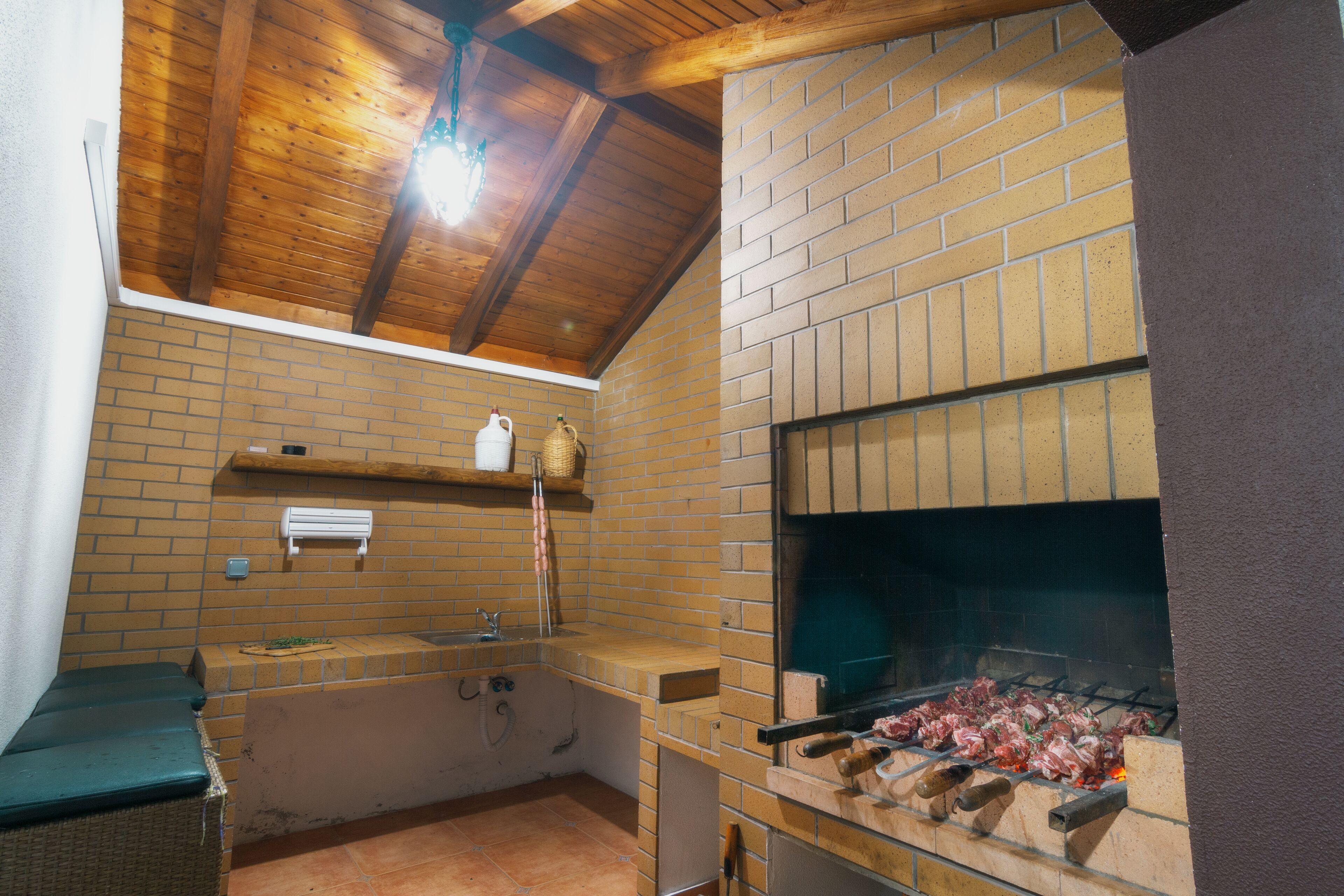 A kitchen with a brick oven, a sink, and a wooden ceiling.