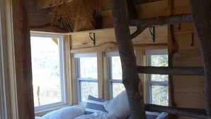 Un dormitorio rústico con cabaña de madera, una cama, una rama colgante y una escalera.