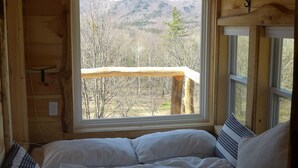 Una habitación de cabaña acogedora, con una cama, un ventanal con vistas a una zona boscosa y paredes de madera.