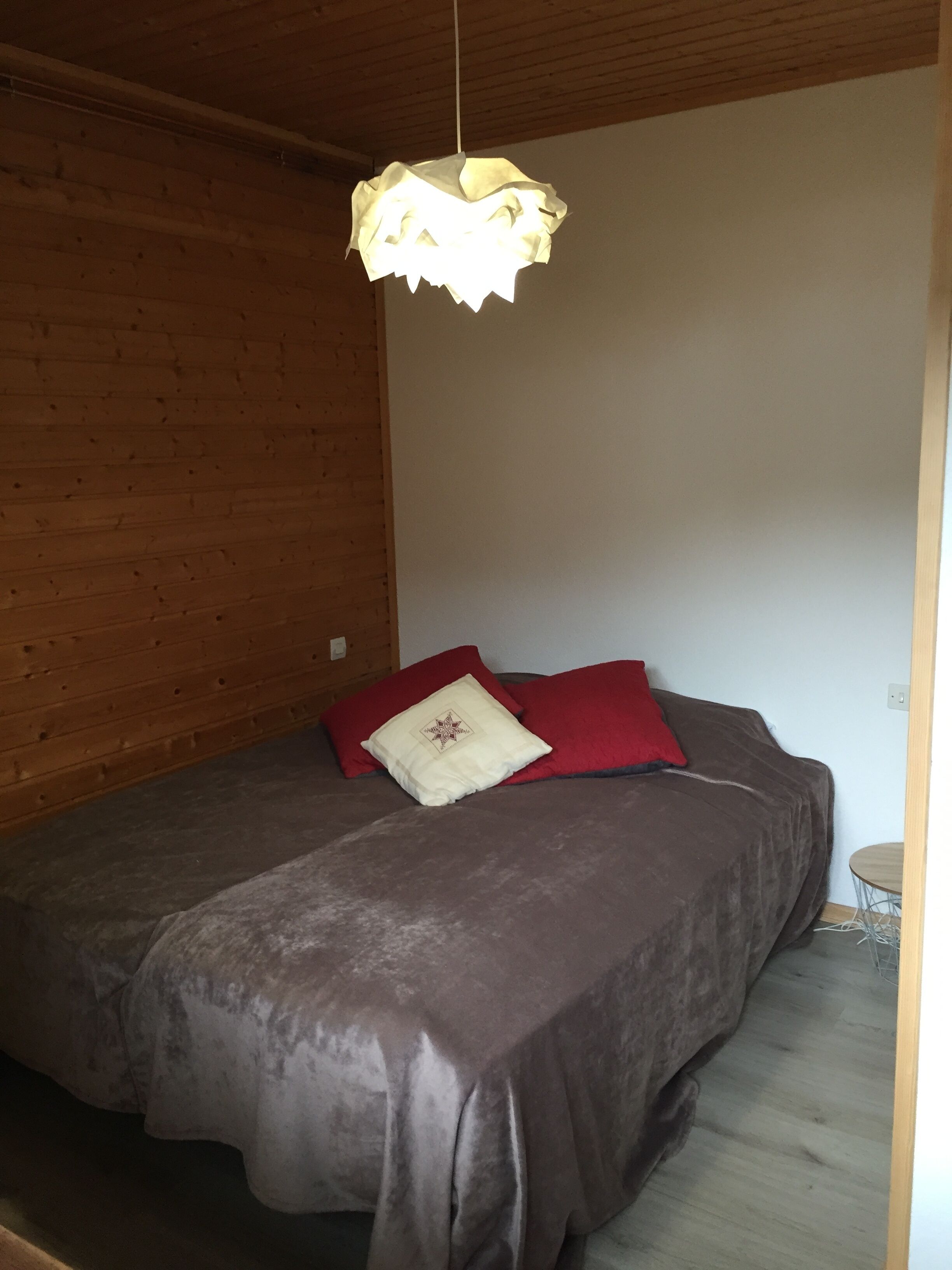 Un dormitorio con techo de madera, una cama con colcha marrón, dos almohadas y una lámpara colgante.