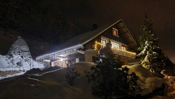 Paisaje nevado con una casa que tiene un balcón y un árbol cubierto de nieve.