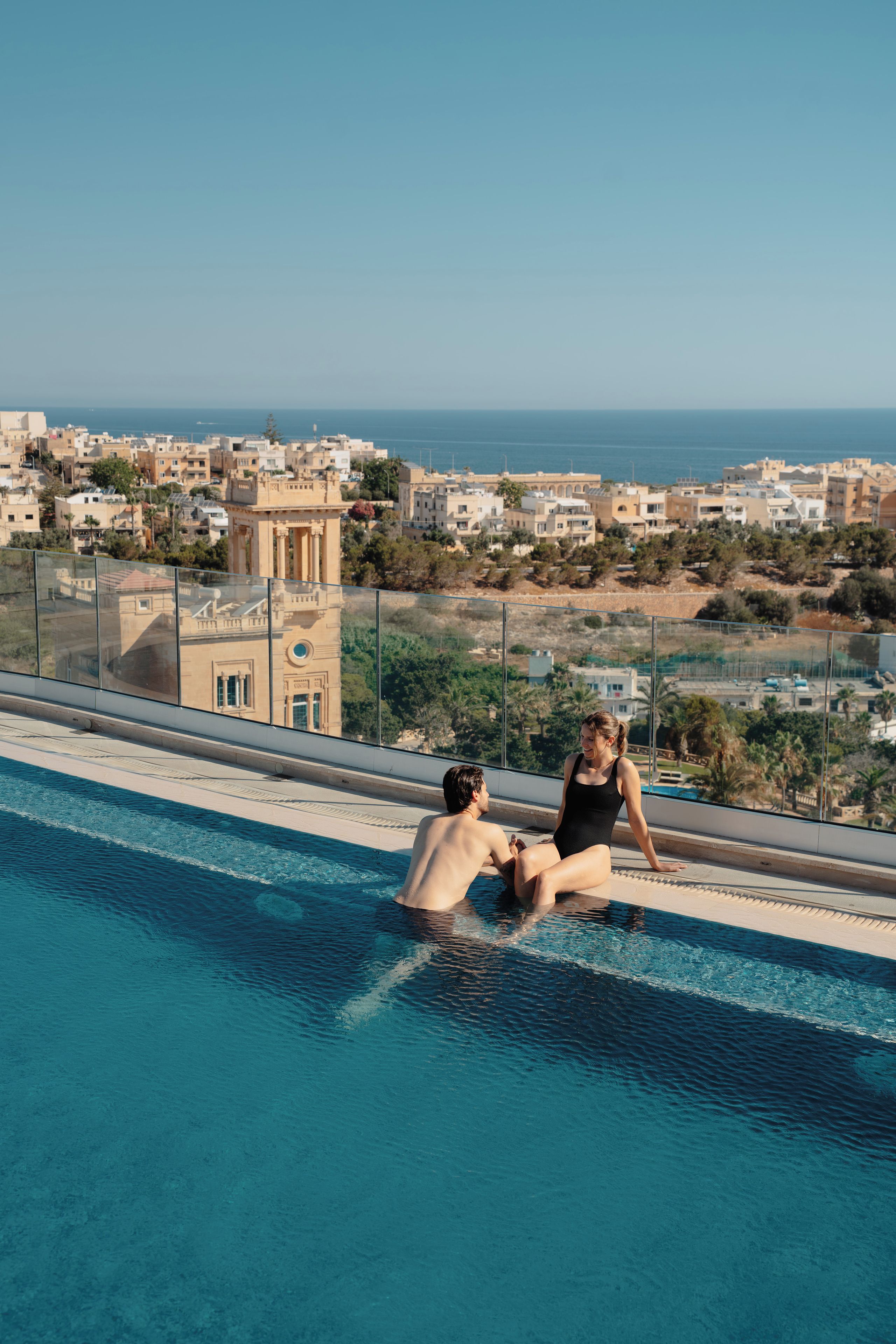 A swimming pool with a view of a coastal town and a historical building.