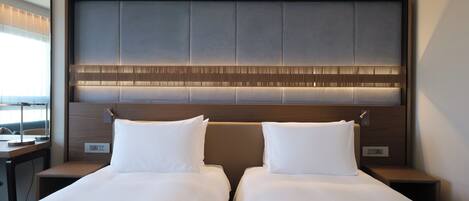 A hotel room with two beds, a wooden headboard, and a bedside table with a lamp.