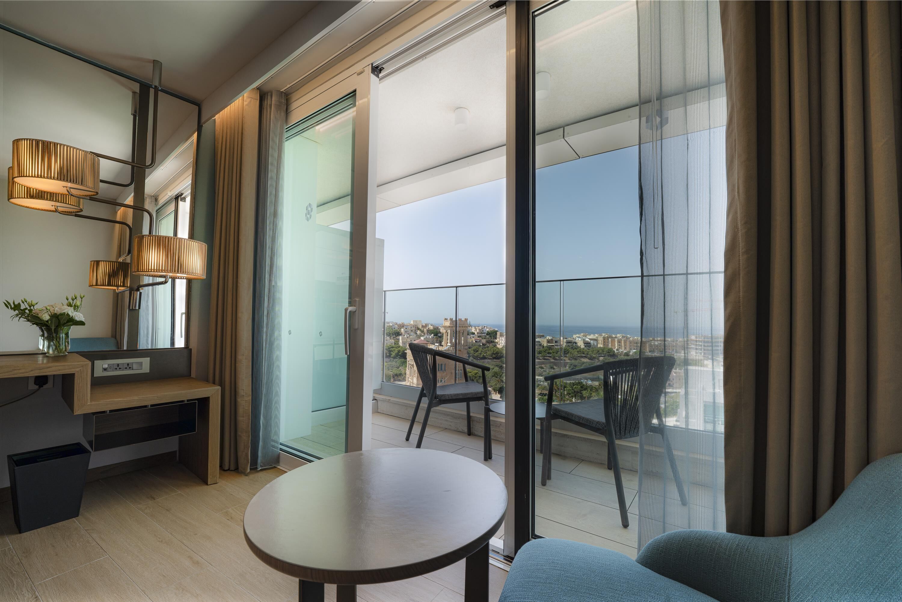 A modern living room with a balcony, a wooden desk, a round table, and a sofa.