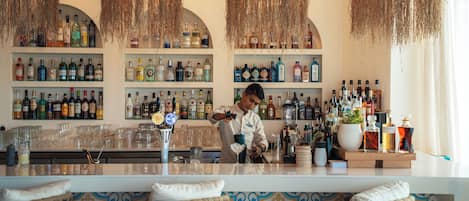 A bar with a bartender preparing drinks, shelves of liquor bottles, and a patterned wall.