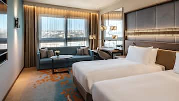 Habitación de hotel con dos camas, un sofá, un escritorio y vista a la ciudad.