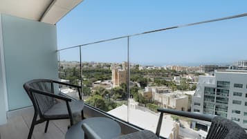 A balcony with two wicker chairs and a small table, offering a view of a cityscape with buildings and a tower.