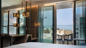 A modern hotel room with a large bed, a desk, and a balcony with a view of the city.