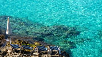 A clear view of a rocky shoreline with three striped beach chairs and a single umbrella.