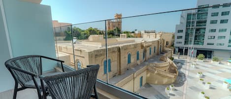 A balcony with two wicker chairs, a view of historic buildings, and a modern building with a sign.