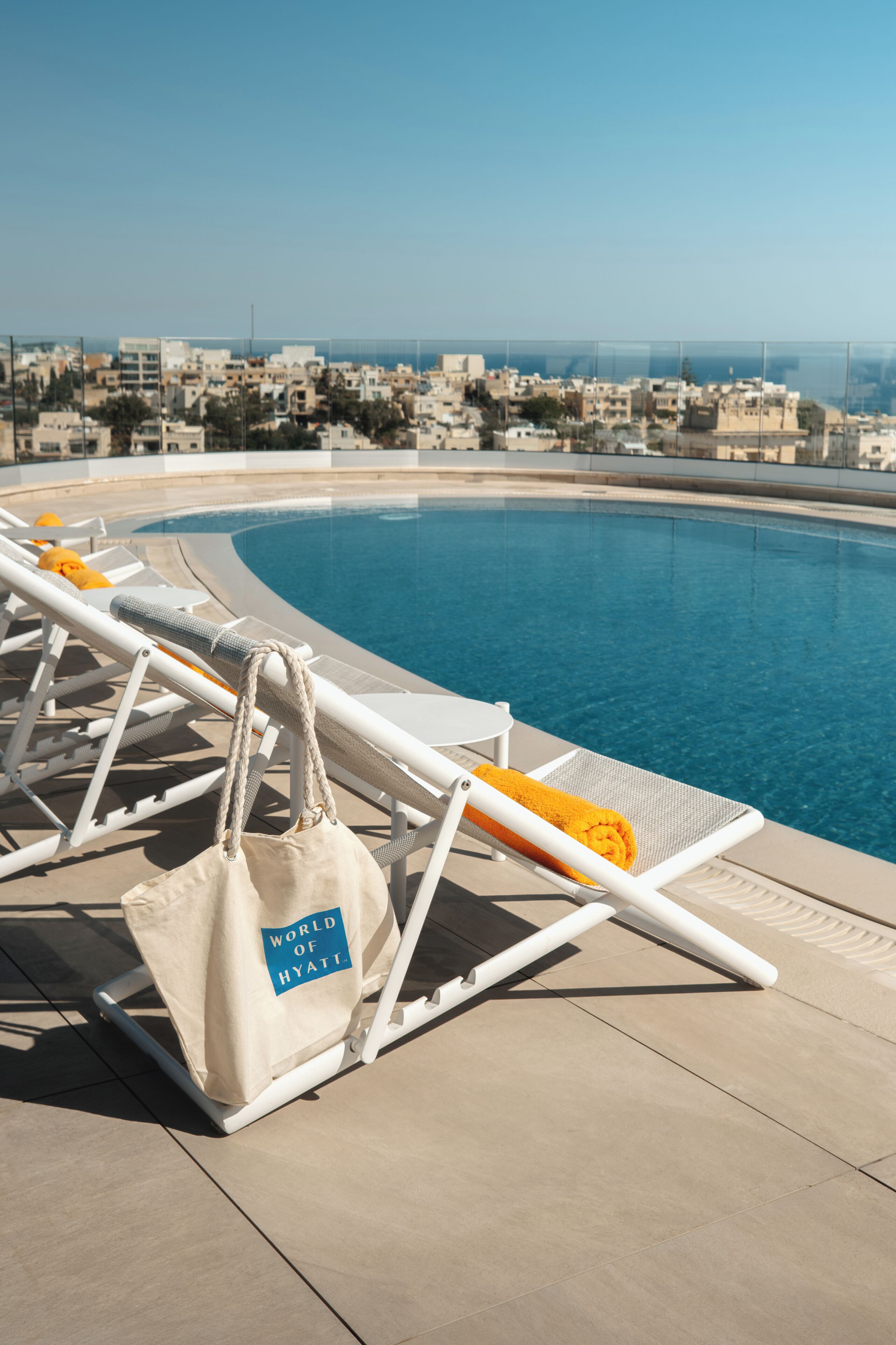 Zona de piscina con sillones reclinables y una bolsa con el logo 'World of Hyatt'.