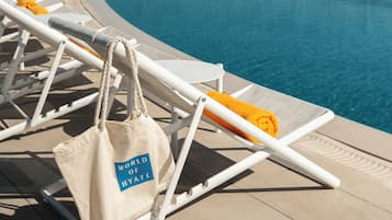 Zona de piscina con sillones reclinables y una bolsa con el logo 'World of Hyatt'.