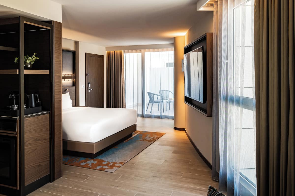 Una habitación de hotel moderna con una cama grande, un armario, un televisor y un balcón con una silla.