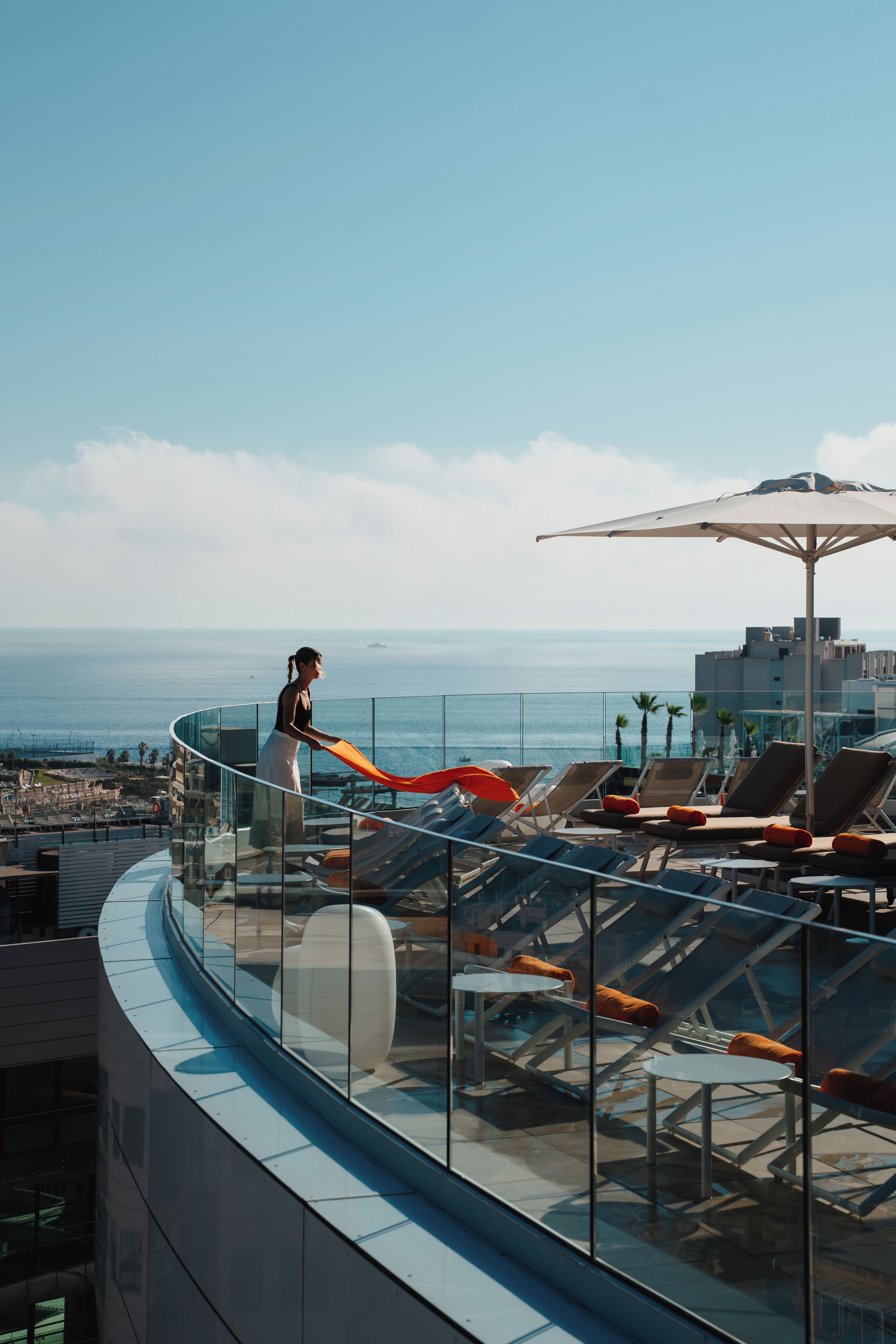 A rooftop terrace with a glass balustrade, lounge chairs, and a view of the sea.