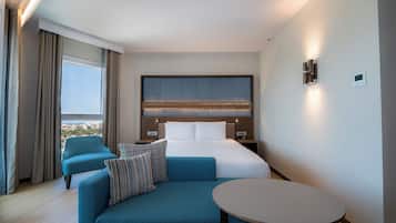 A modern hotel room with a large bed, a sofa, a small table, and a view of the city.