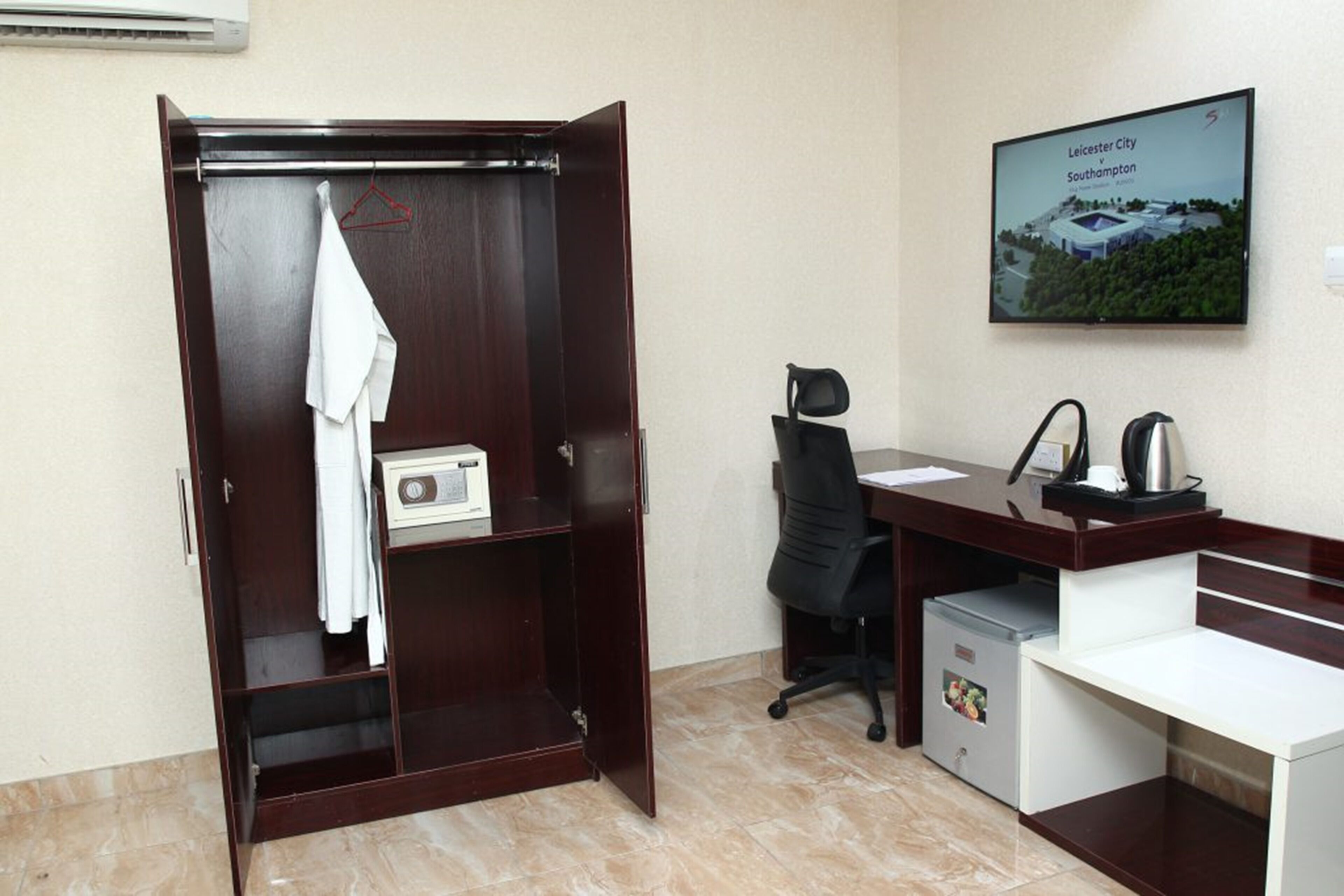 A hotel room with a wooden wardrobe, a desk with a chair, a coffee maker, and a framed picture on the wall.