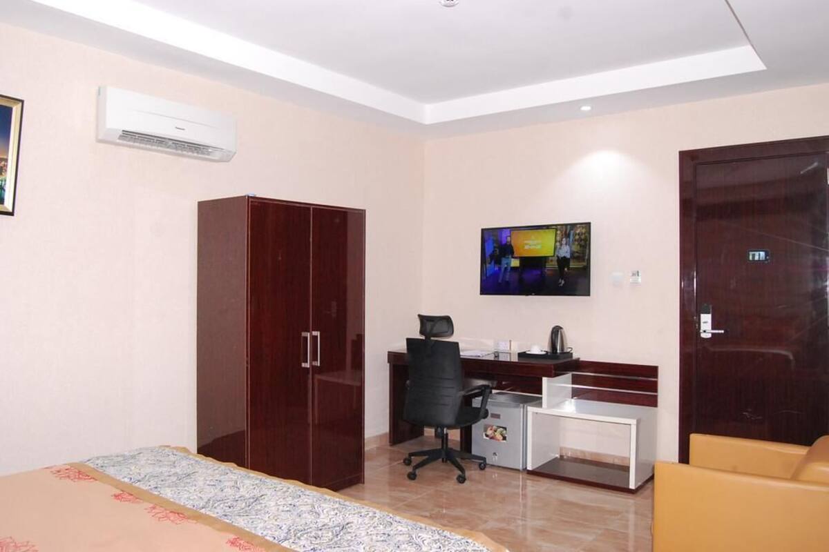 A hotel room with a bed, a desk with a computer, a TV, and a wardrobe.
