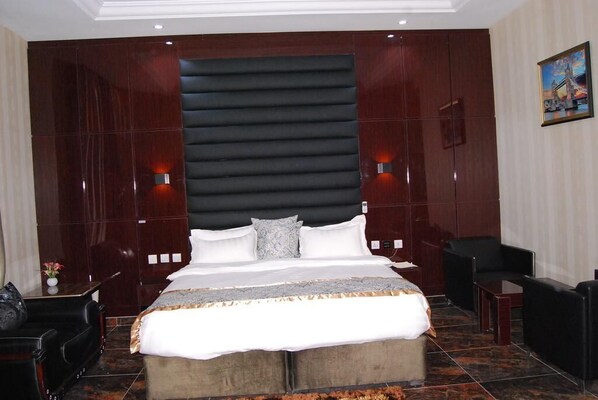 A hotel room with a large bed, two bedside tables, a chair, and a small table. - Exclusive Serene Hotel (Enugu)