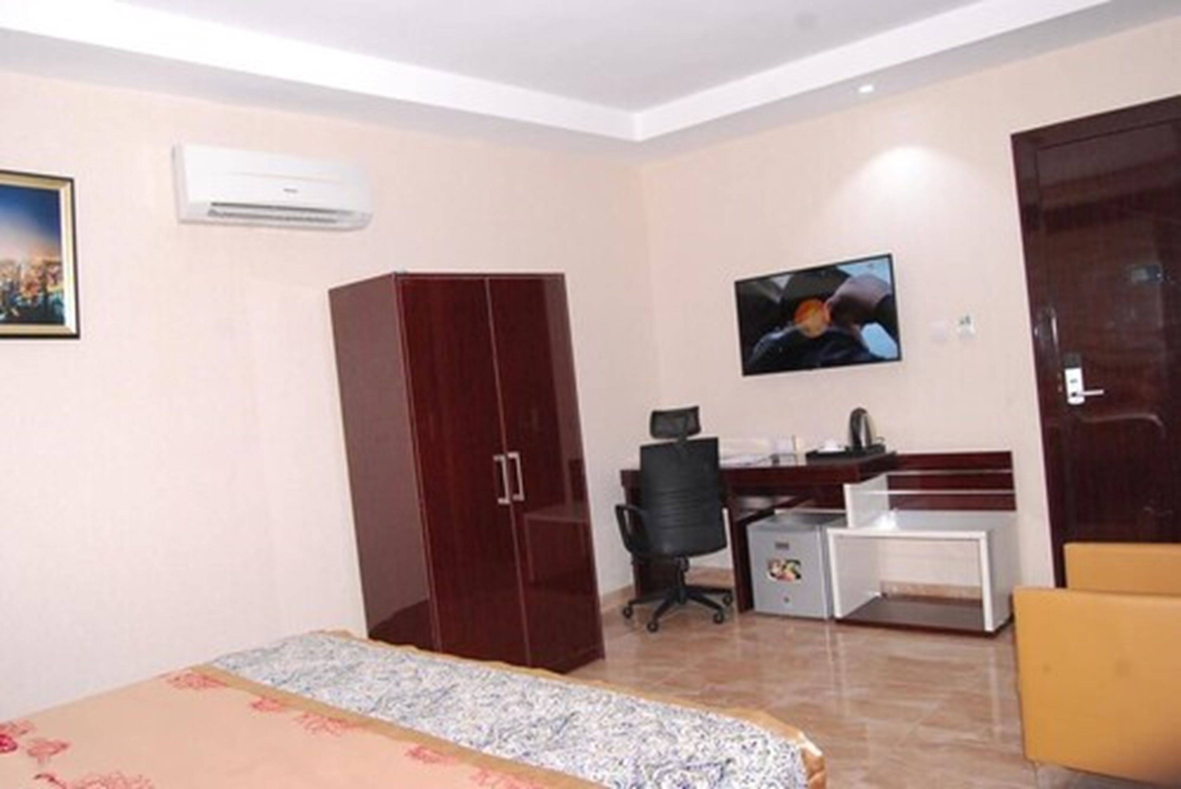A hotel room with a bed, wardrobe, desk, chair, television, and air conditioning unit.