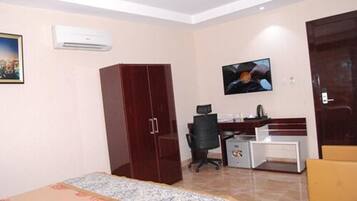 A hotel room with a bed, wardrobe, desk, chair, television, and air conditioning unit.