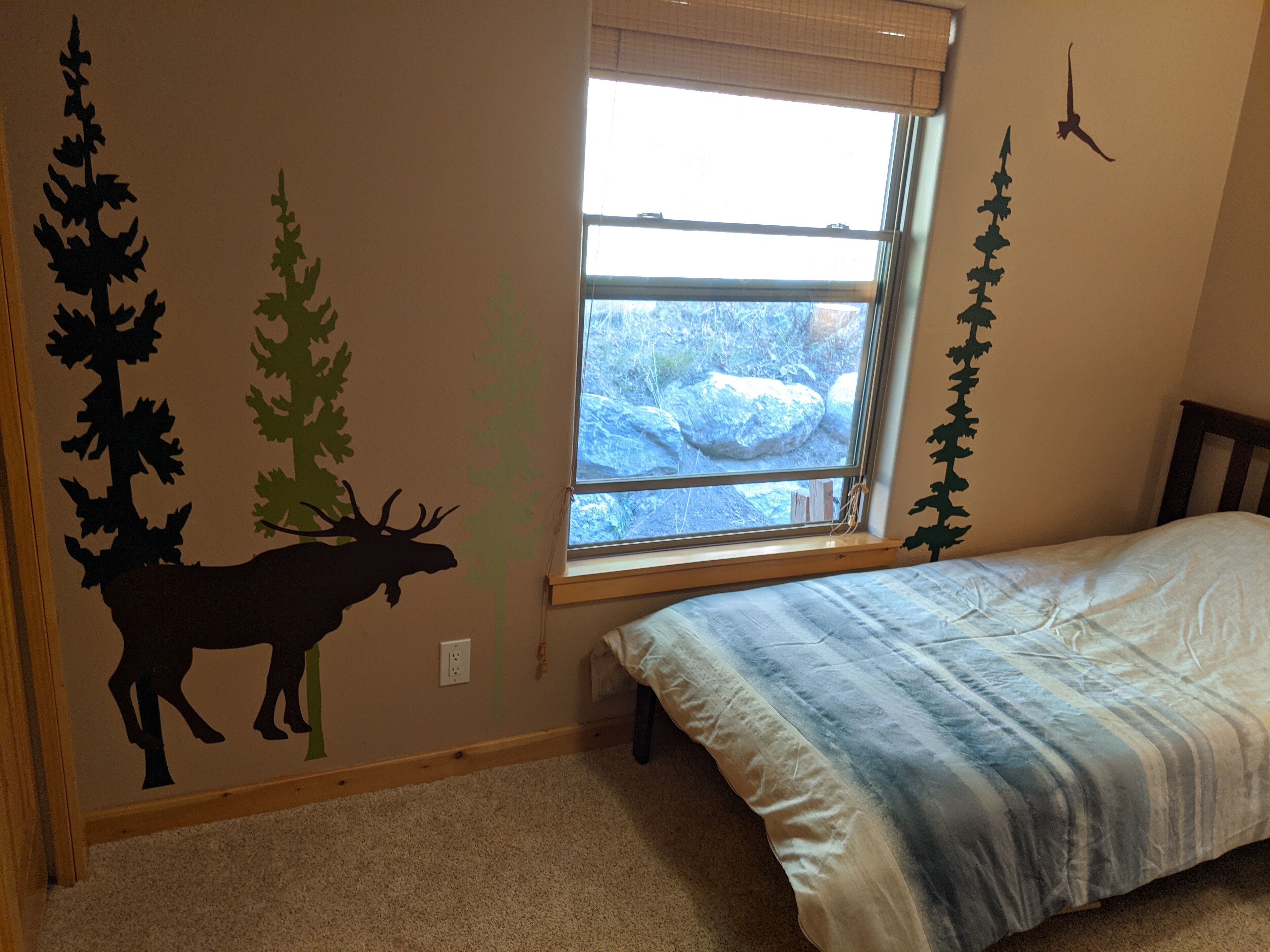 Quarto com cama, janela com vista para rochas e adesivos de parede com árvores e um alce.