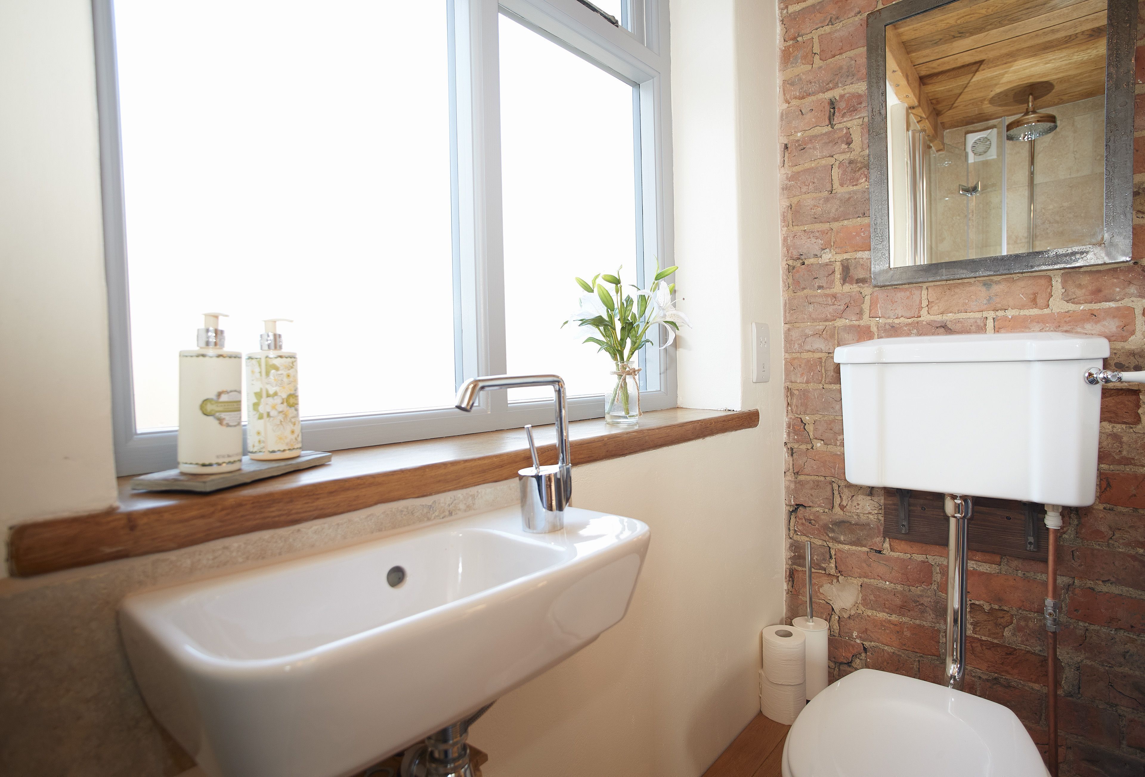 A bathroom with a white sink, a window above it, and a brick wall.