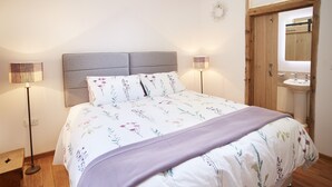 Un dormitorio con cama, lámparas de noche, piso de madera y una puerta de madera que da al baño.